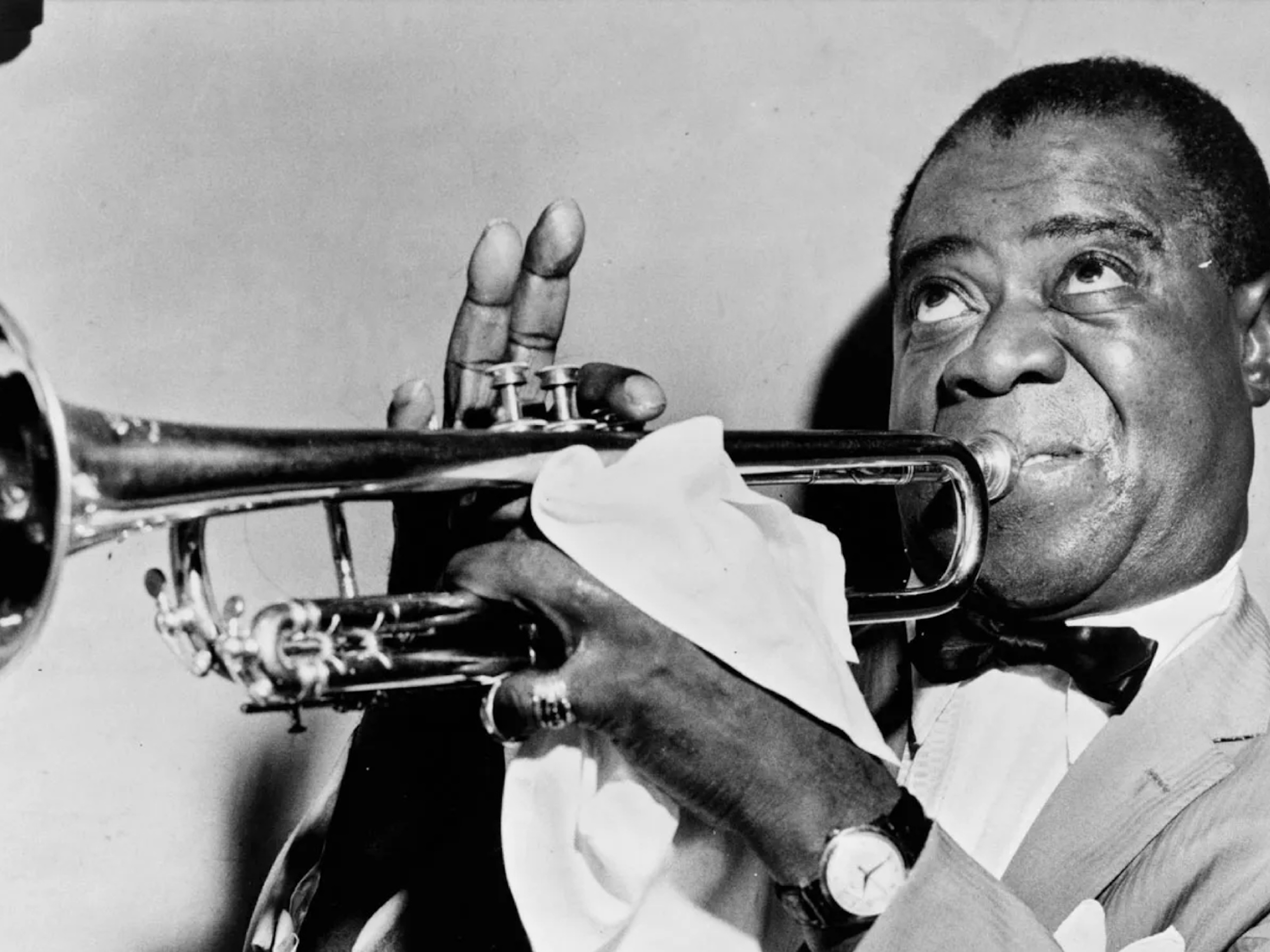 An archival photo of Louis Armstrong playing the trumpet.