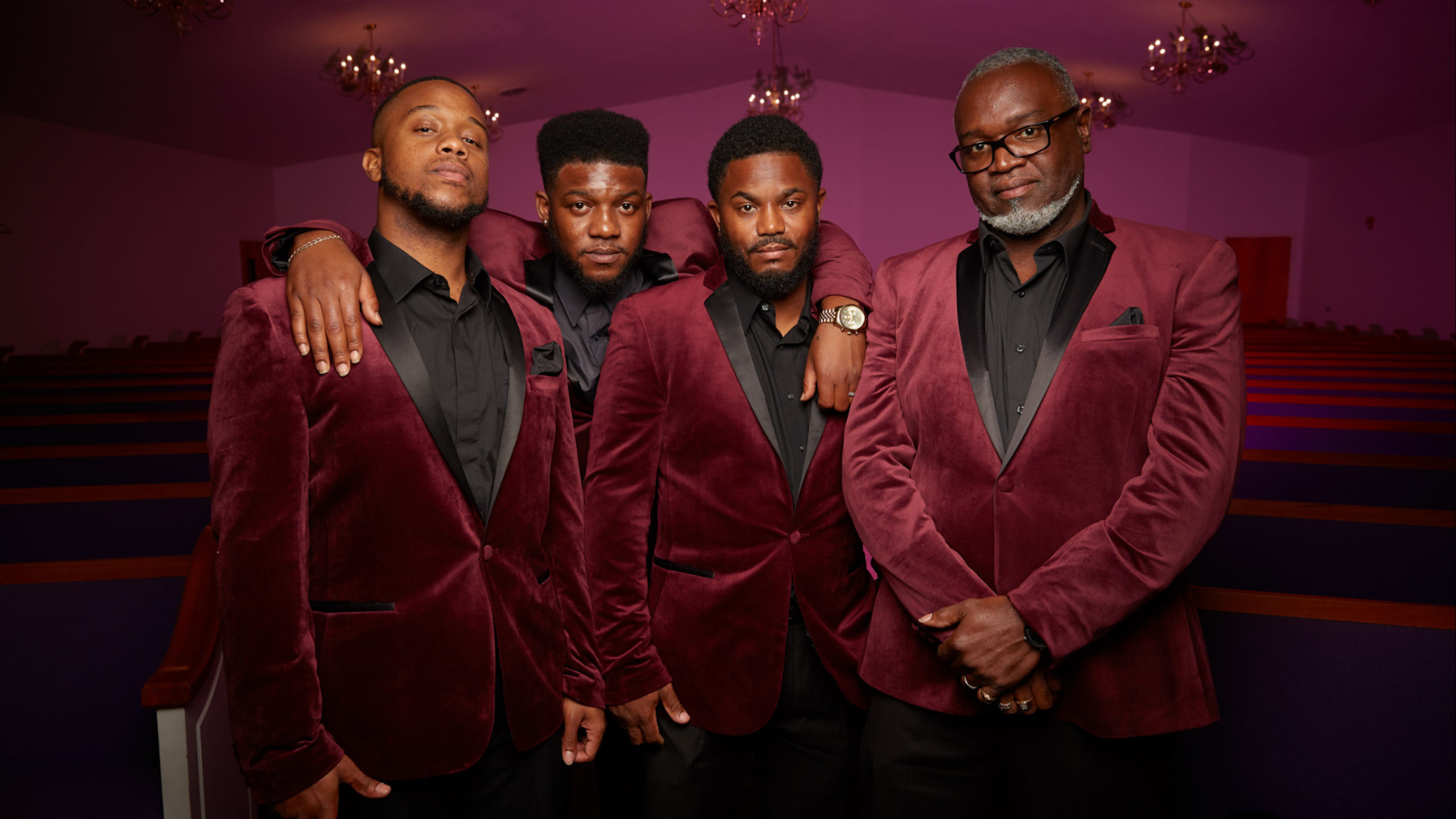 A Group of Musicians stand closely together in a small church.