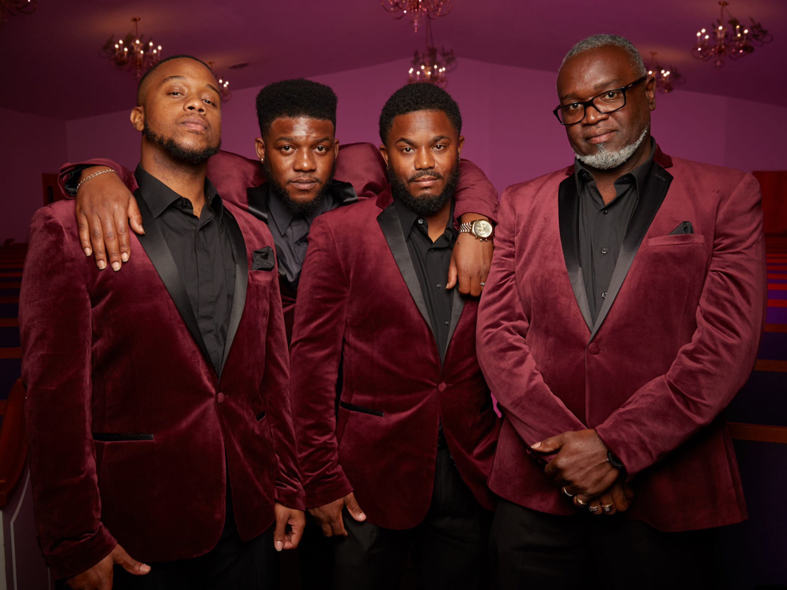 A Group of Musicians stand closely together in a small church.