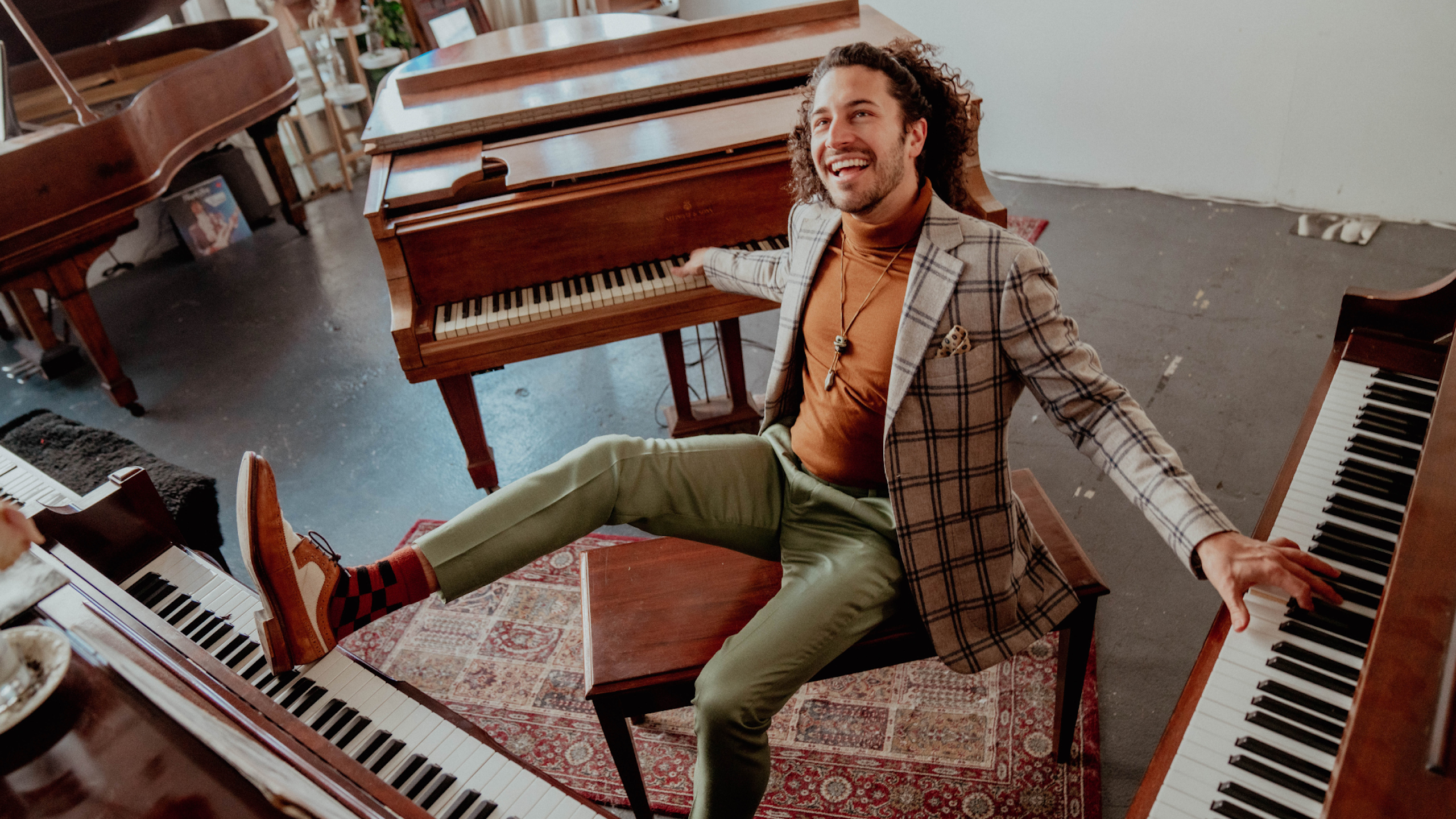 A man sits on a bench surrounded by 3 pianos. He is playing the pianos with hands and his feet.