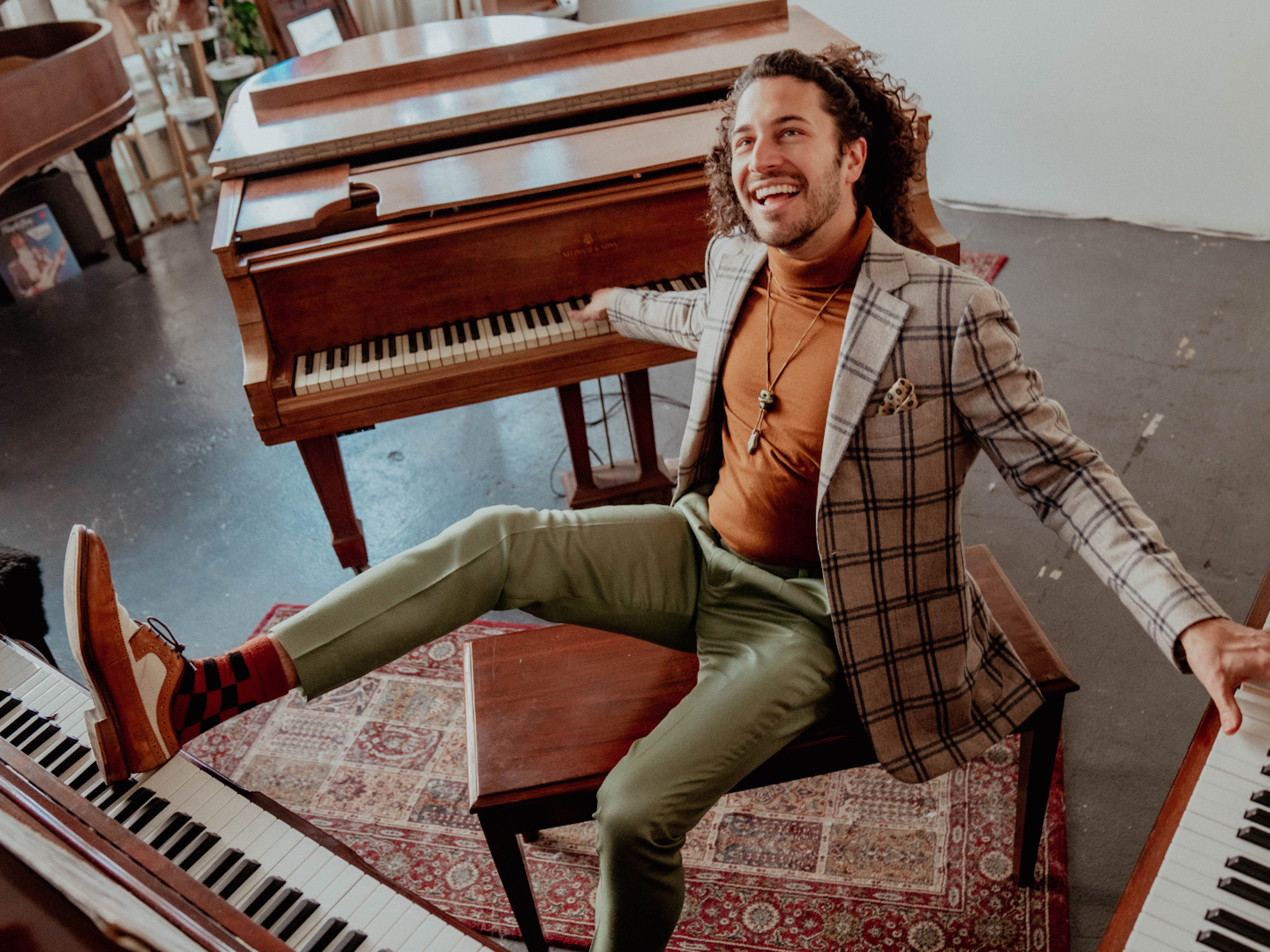 A man sits on a bench surrounded by 3 pianos. He is playing the pianos with hands and his feet.