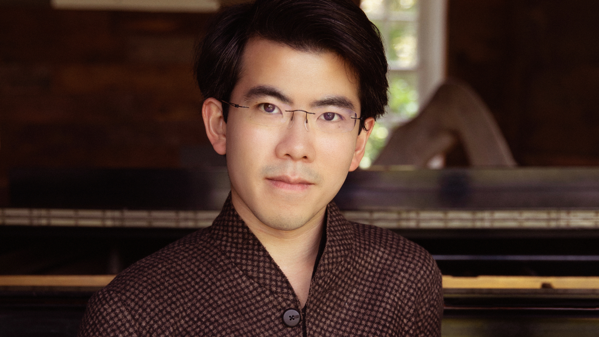 A close up head shot of a man standing in front of a piano.