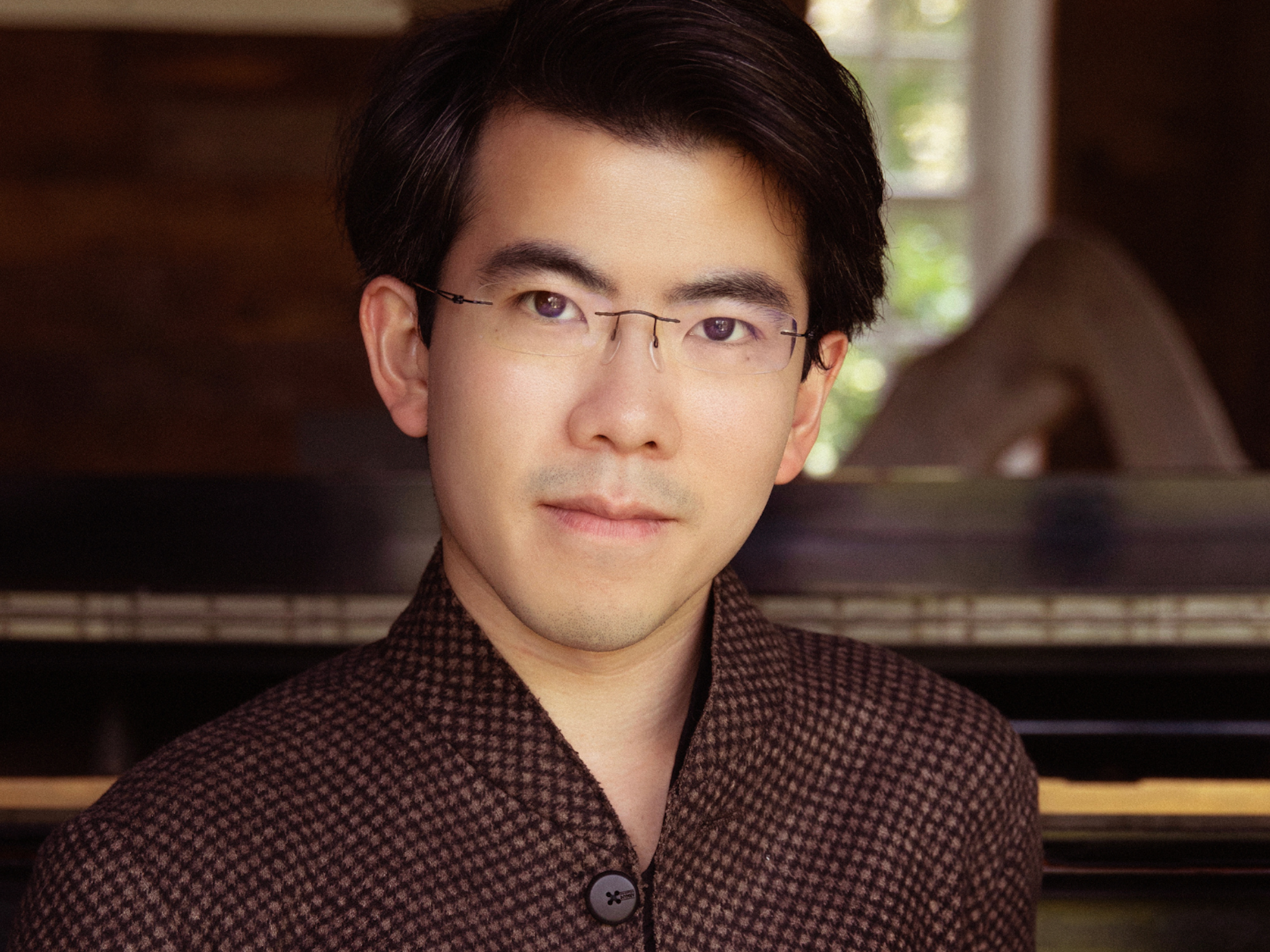 A close up head shot of a man standing in front of a piano.
