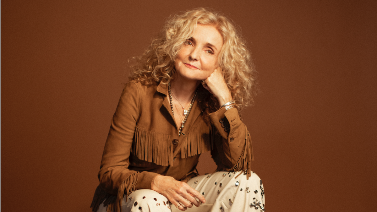 A woman in a fringe blouse sits forward on a box.
