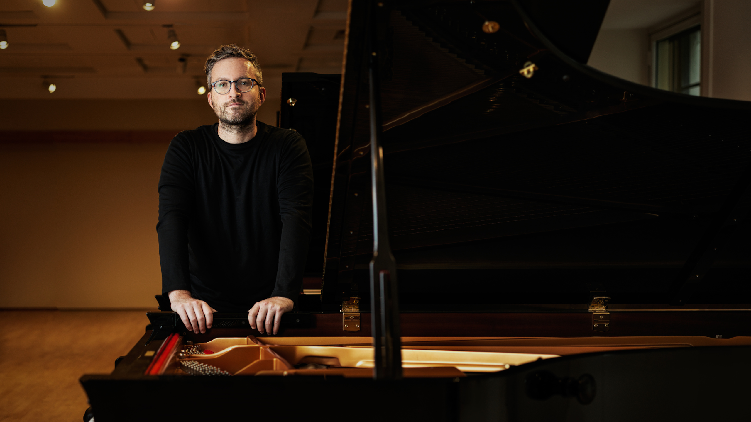 A man stands with his hands holding an open piano.