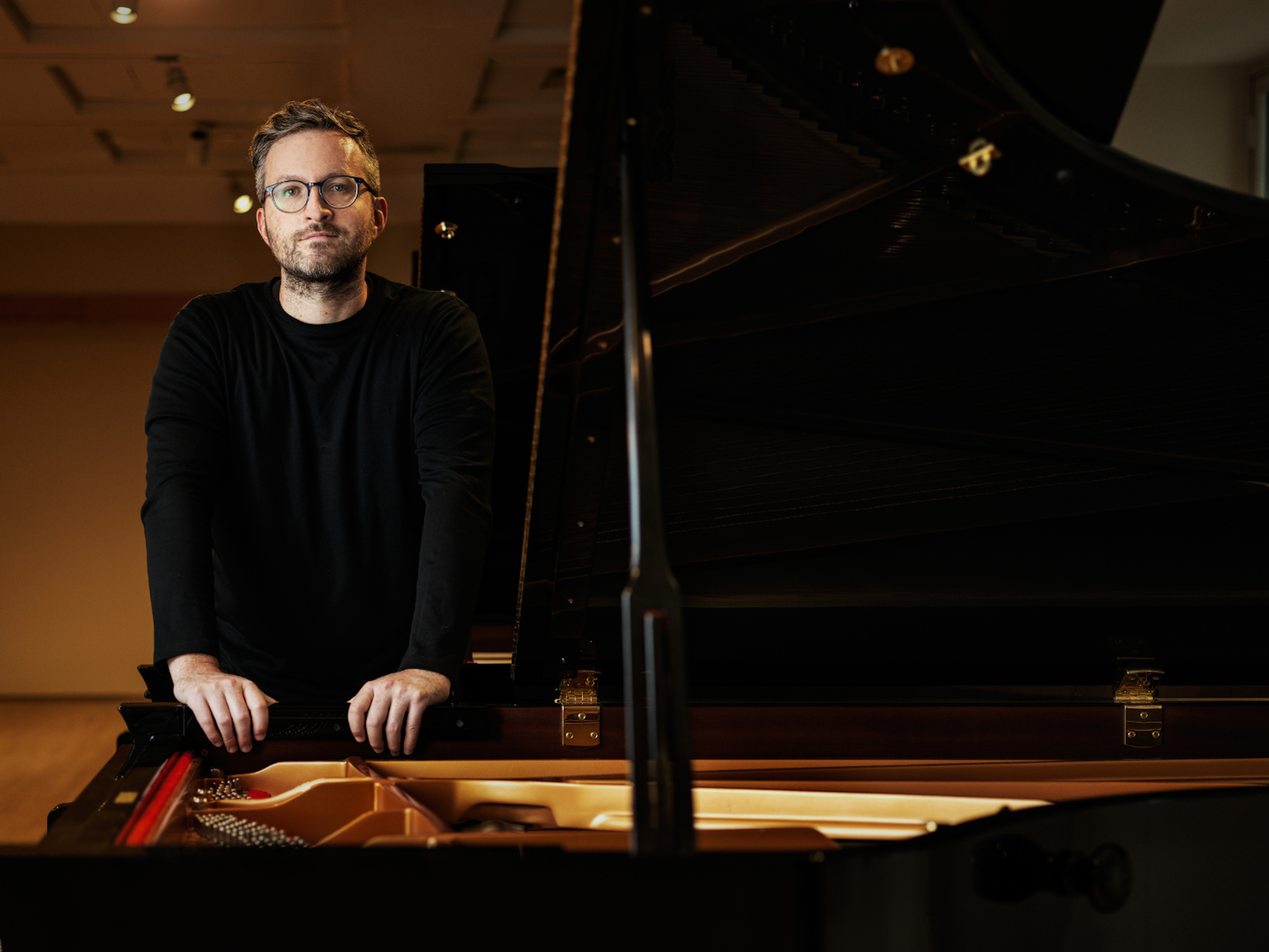 A man stands with his hands holding an open piano.