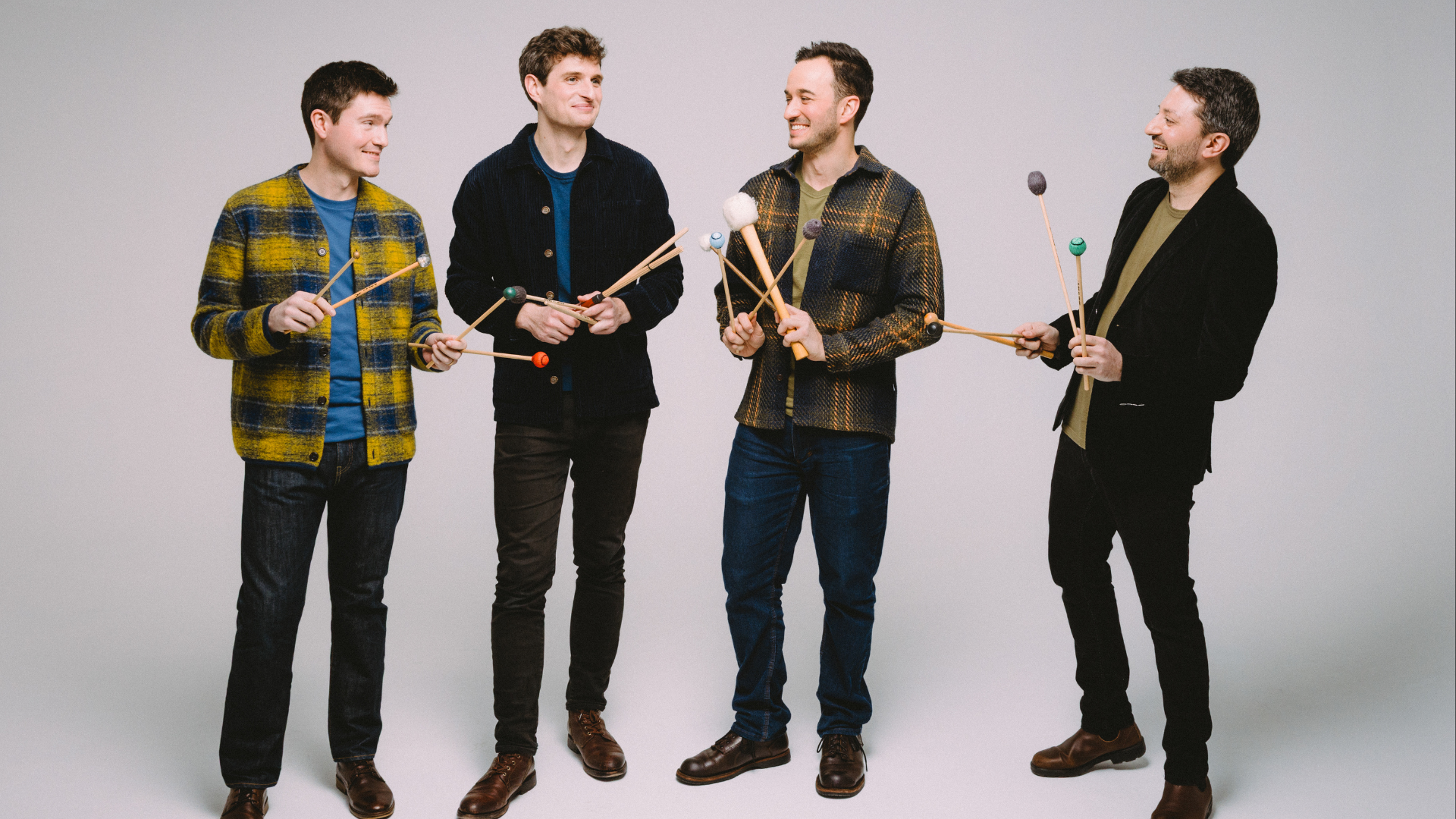 A group of musicians look at each other while holding 4 xylophone mallets each in their hands.