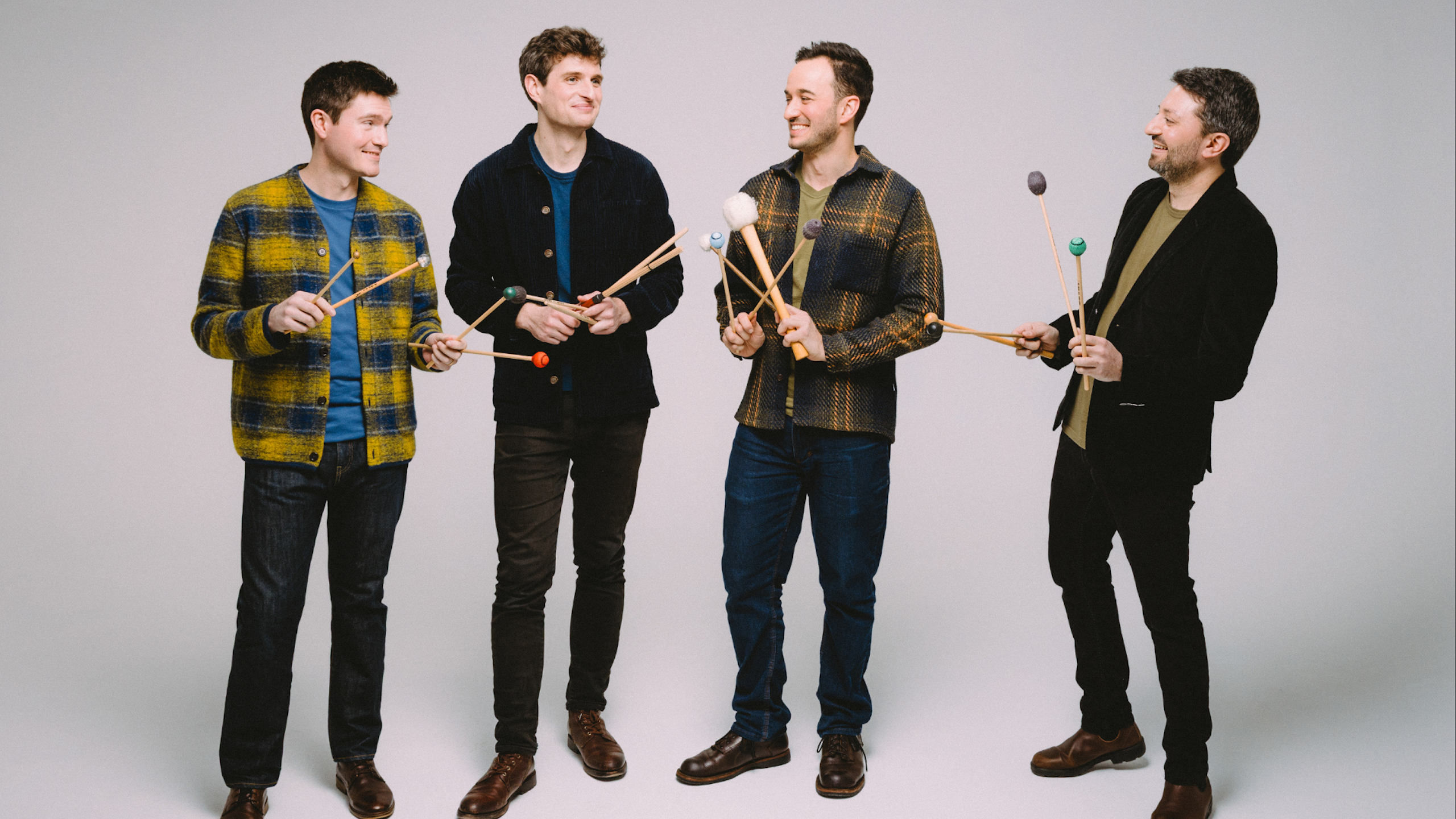 A group of musicians look at each other while holding 4 xylophone mallets each in their hands.