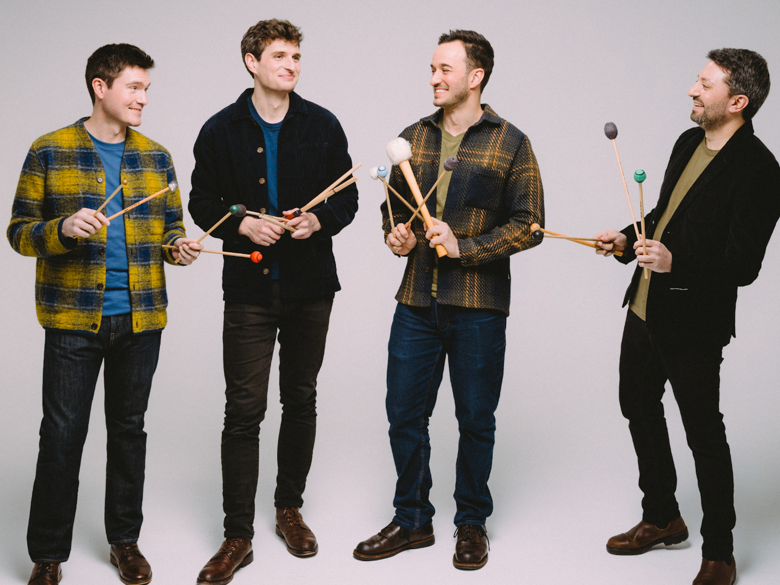 A group of musicians look at each other while holding 4 xylophone mallets each in their hands.