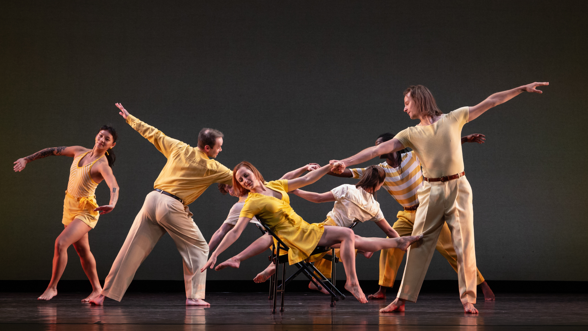 7 musicians hold a pose on stage. Dancers hold hands with eachother.