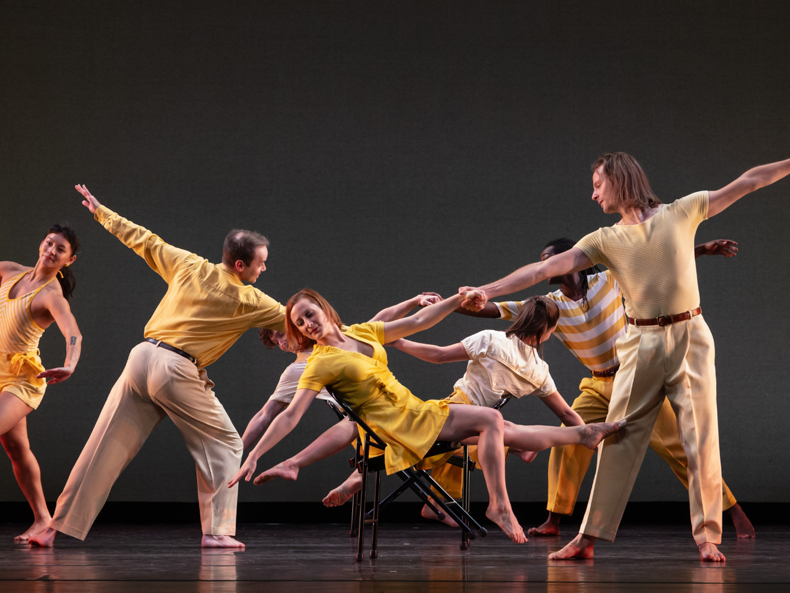 7 musicians hold a pose on stage. Dancers hold hands with eachother.