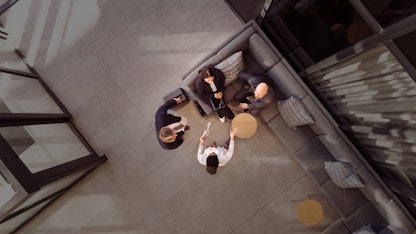 Four people are meeting in a bright, modern office space. Two men are standing while a man and woman sit and converse