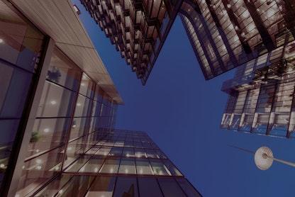 Multiple modern glass buildings stand tall against a dark blue sky