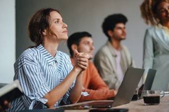 A group of men and women listen attentively as they sit next to laptops with a coffee