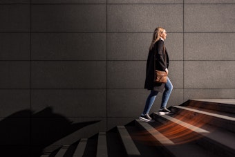 A woman in a coat with a brown leather bag climbs a set of stairs