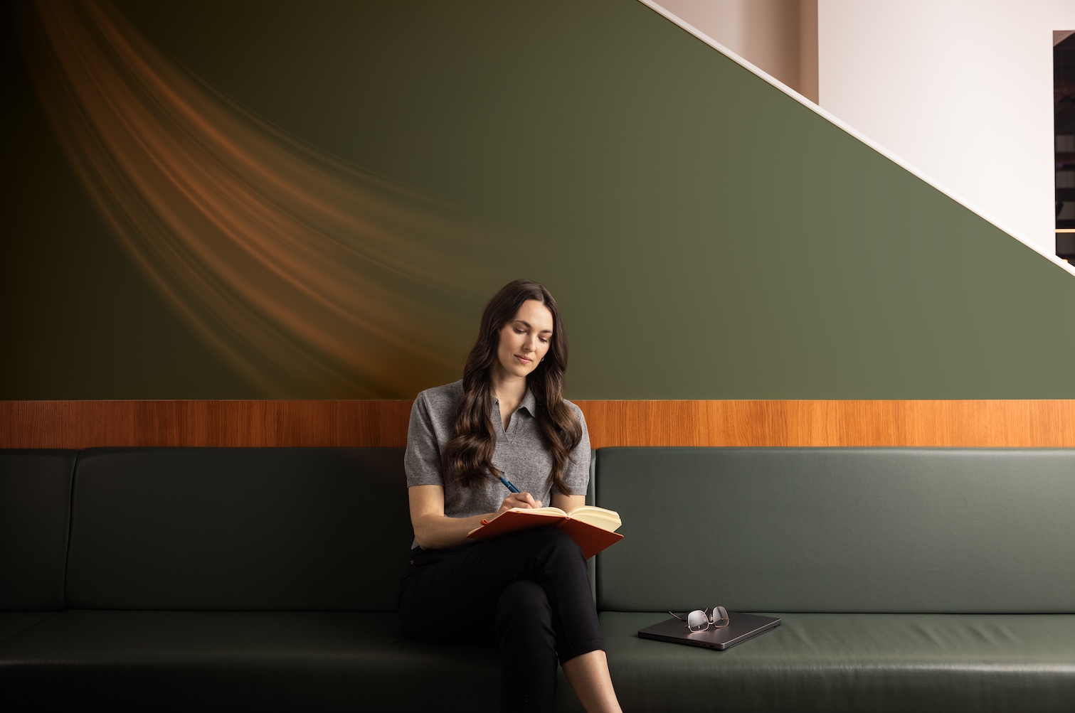 A woman sits on a green sofa writing in a notebook