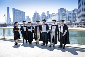 A group of young graduates stand at Sydney harbour on a clear day