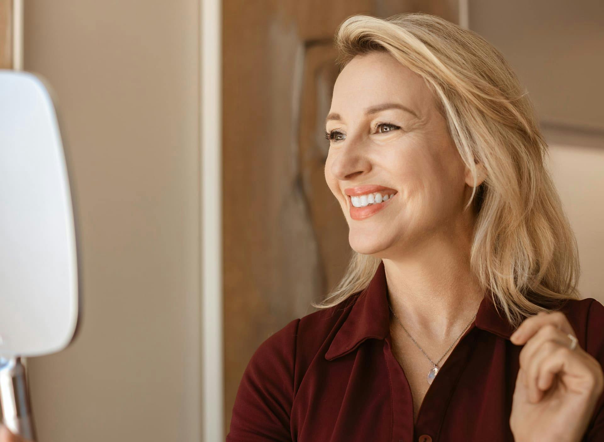 woman smiling while looking in handheld mirror