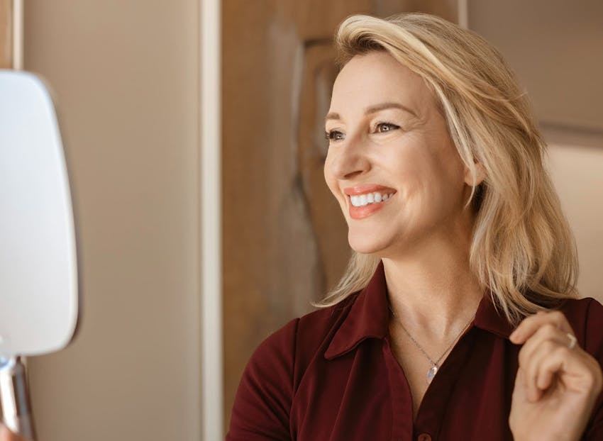 woman smiling while looking in handheld mirror