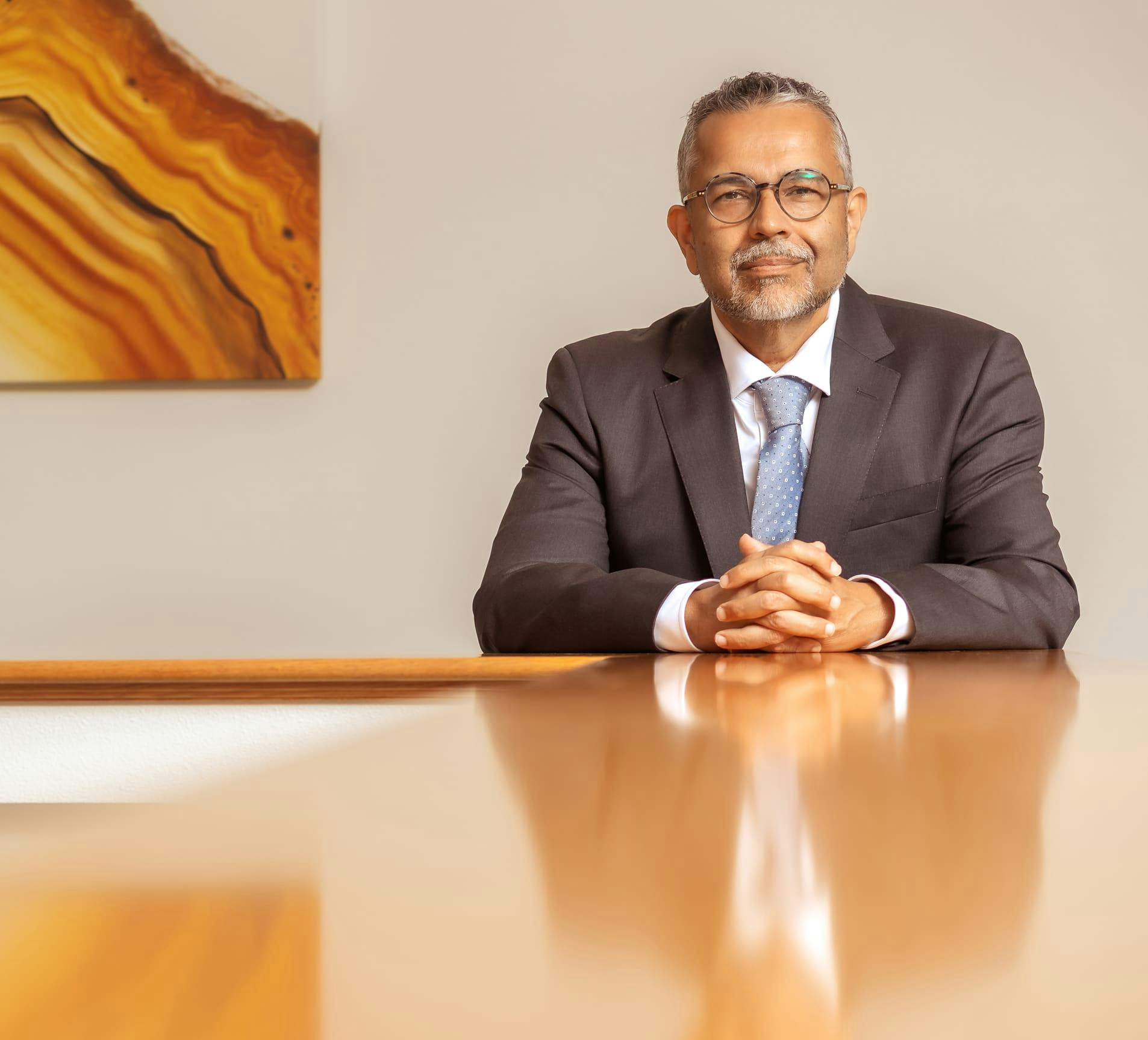 Dr. Munish Batra smiling while sitting at table with his hands together