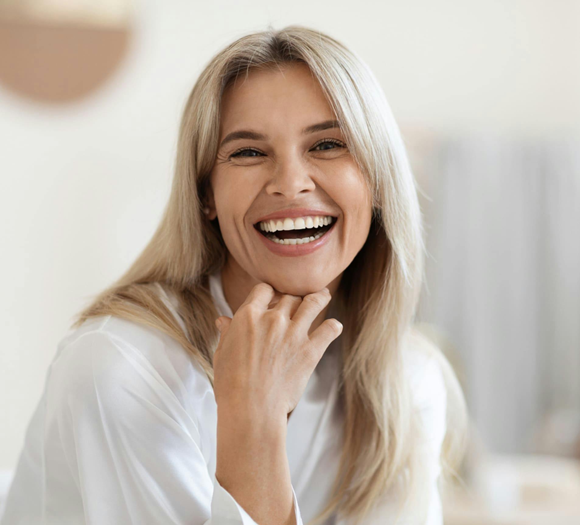 woman with blonde hair smiling with her hand under chin