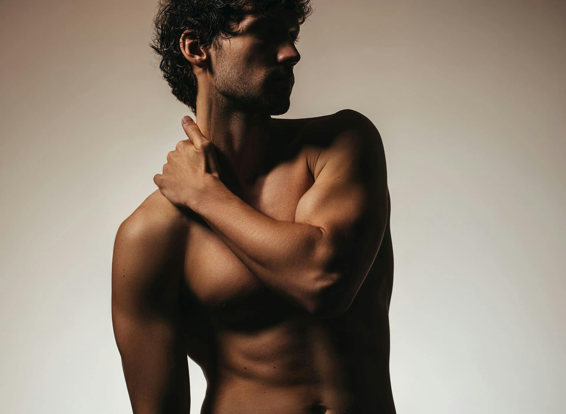 man posing shirtless with his arm on his shoulder