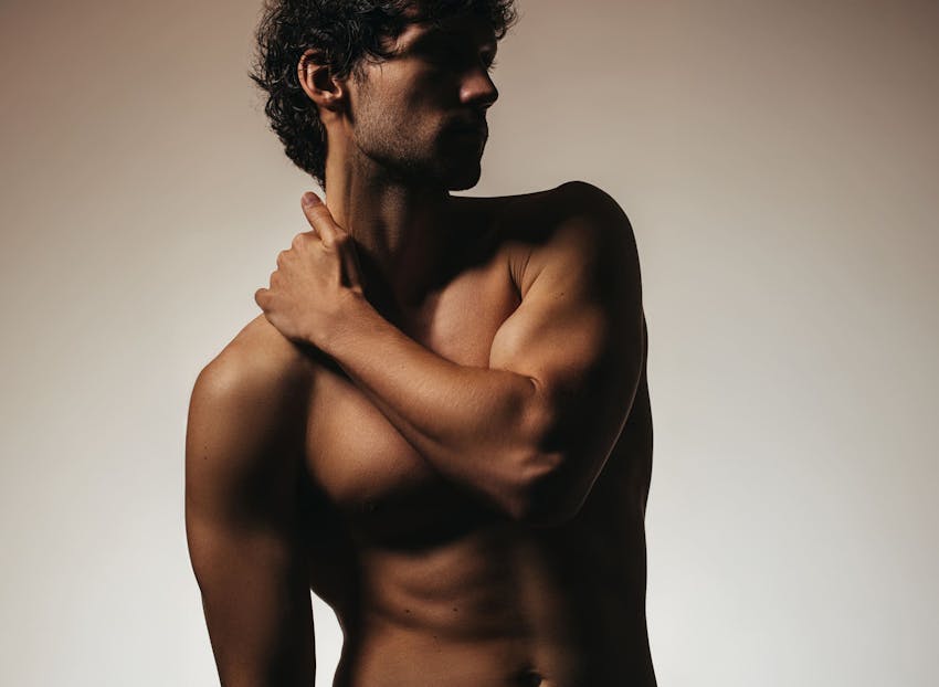 man posing shirtless with his arm on his shoulder