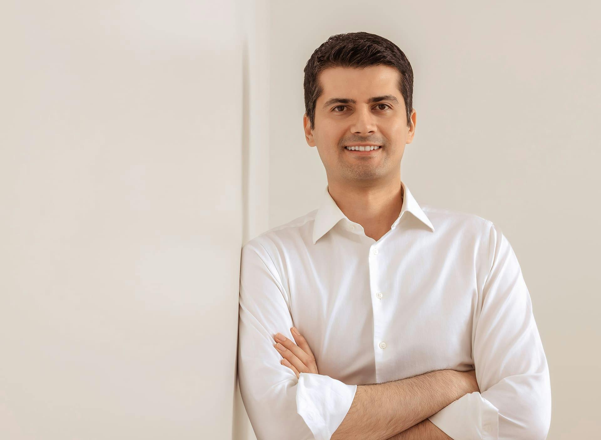 Dr. Cagri Cakmakoglu smiling with his arms crossed while leaning against the wall