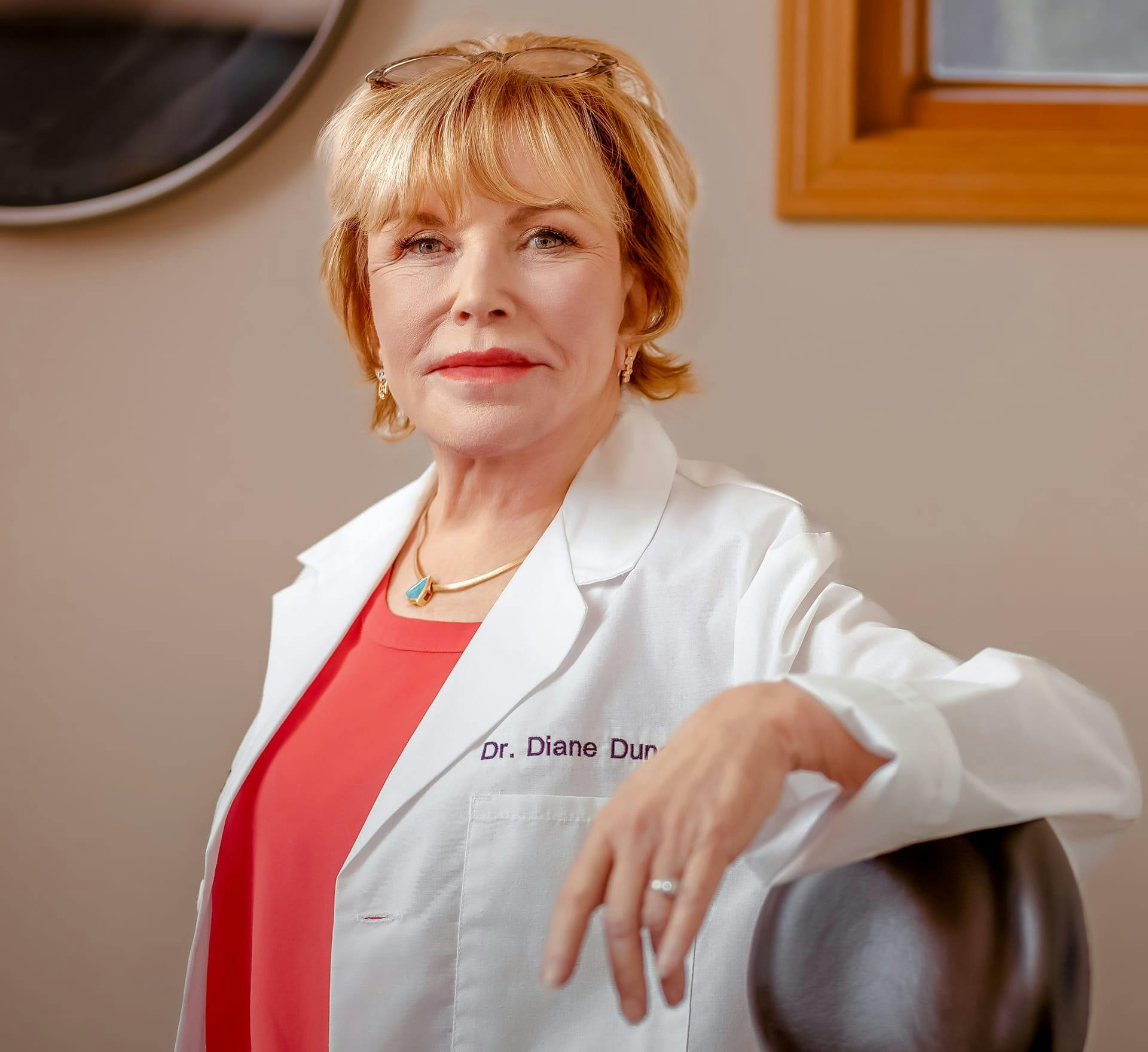 Dr. Diane Duncan in pink shirt and lab coat with hand propped up on medical chair