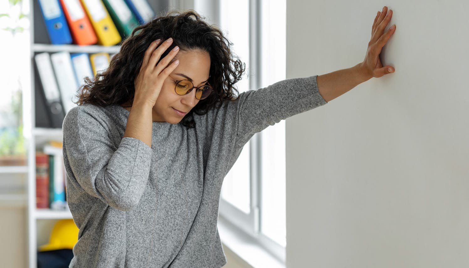 woman holding her head and leaning against a wall