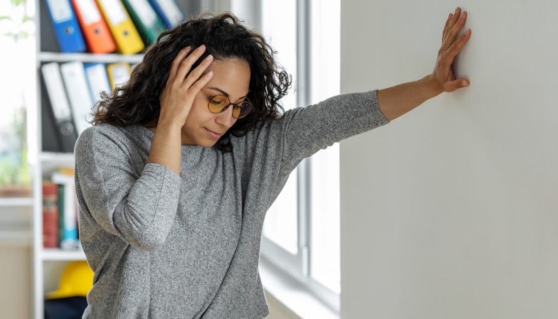 woman holding her head and leaning against a wall