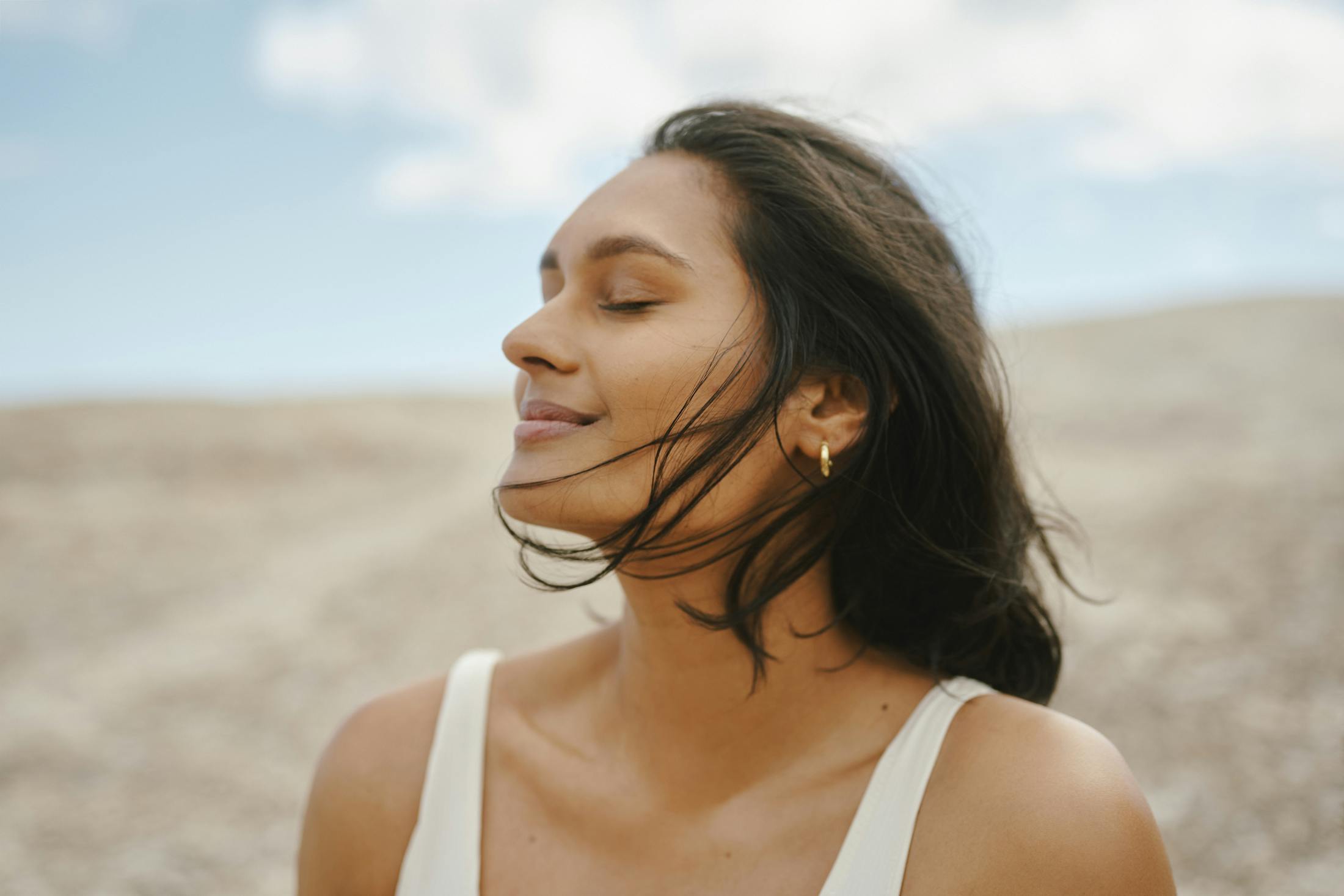 Woman smiling with eyes closed on a dirt hill taking in the fresh air and sun.