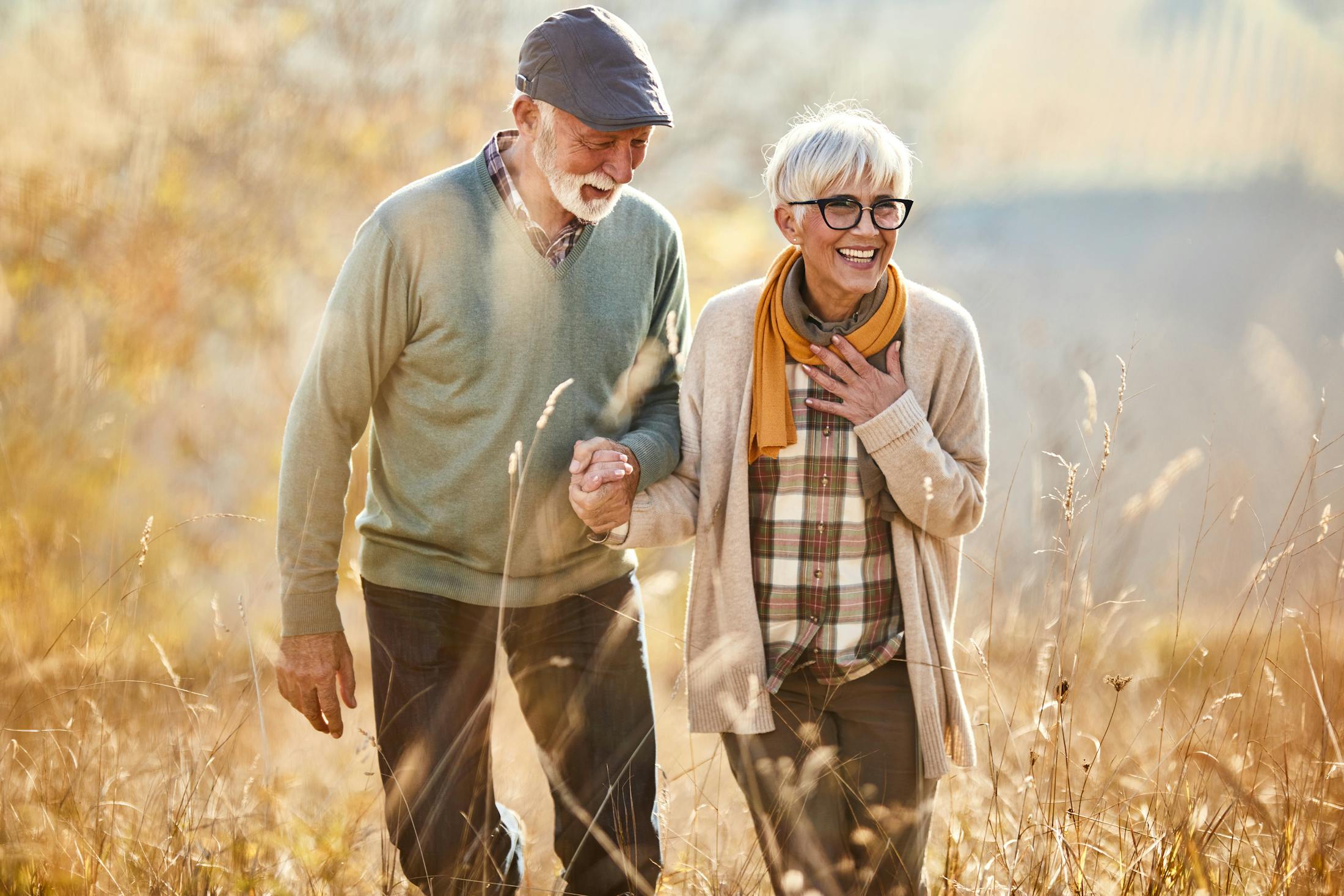 older woman and man dressed in fall clothing walking through a field