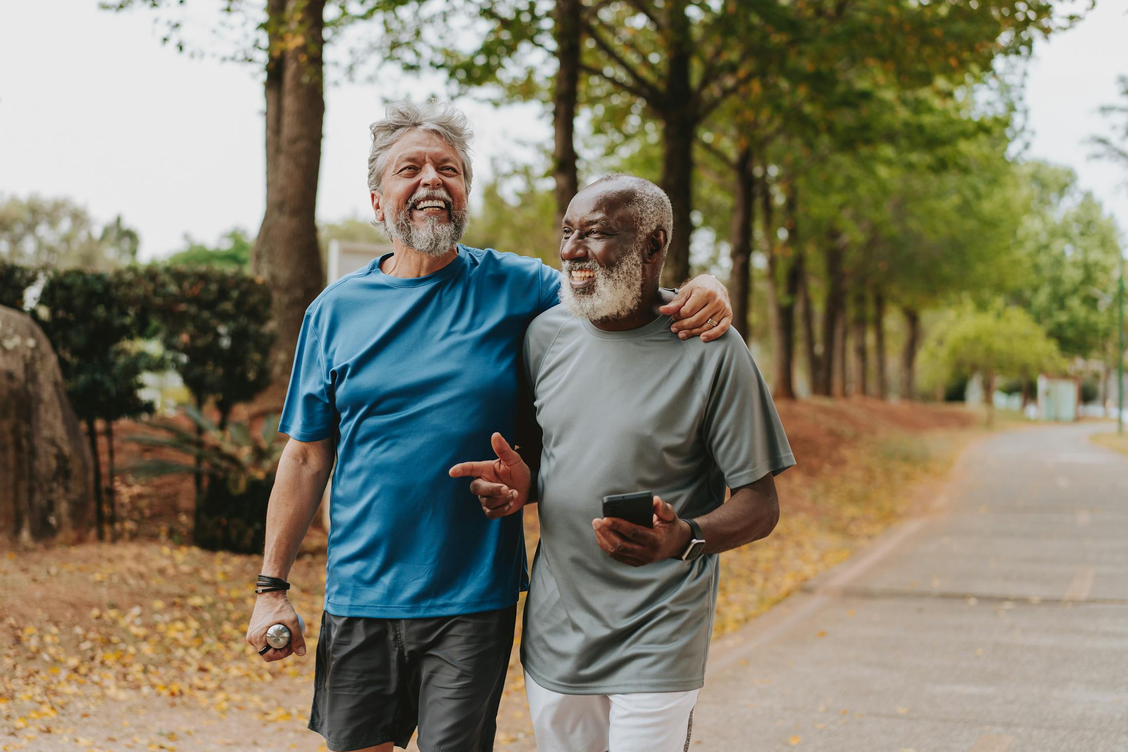 two older men walking in a park and laughing. They are in exercise clothes