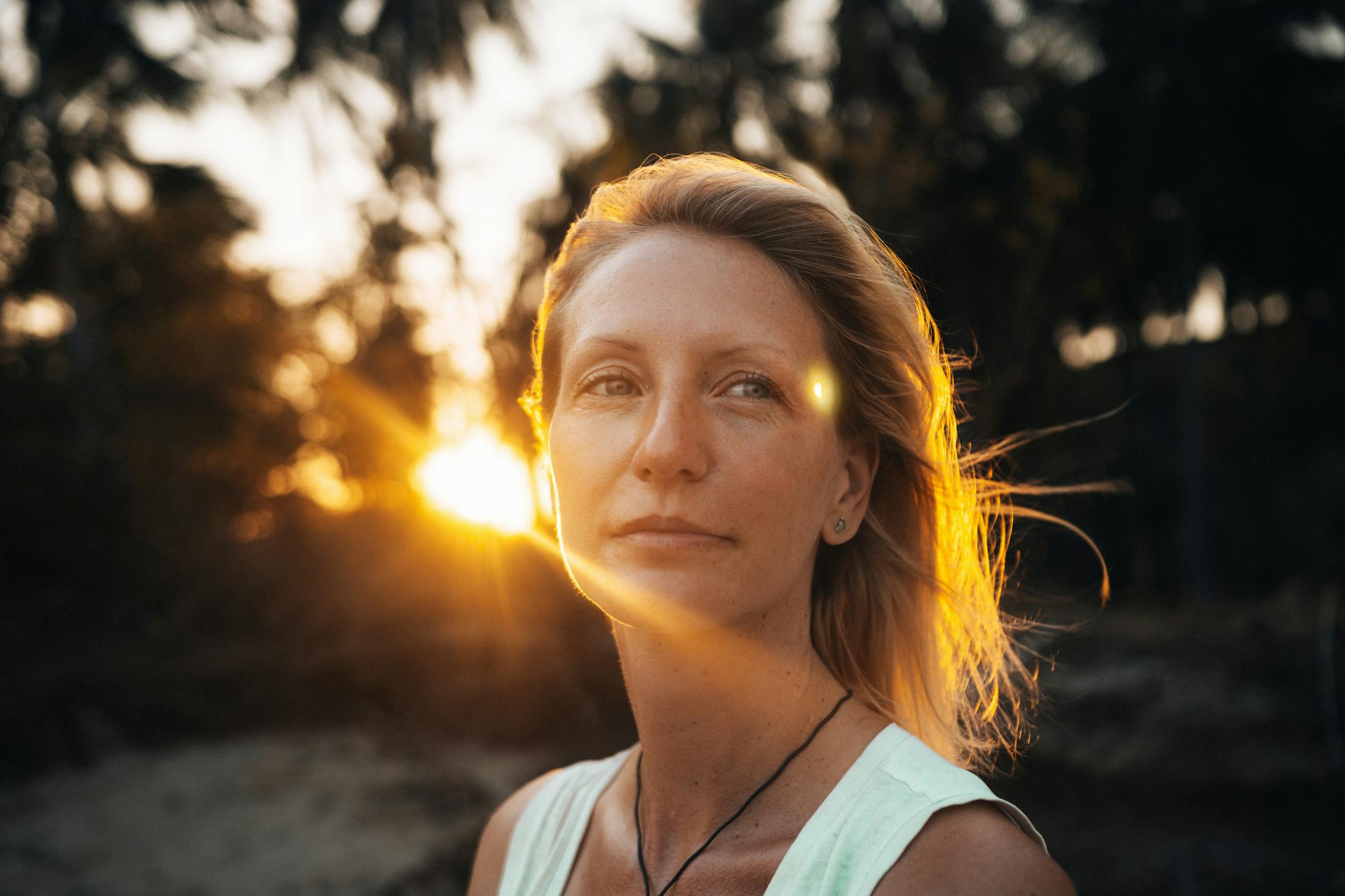 woman looking off content. She is outside at Sunset as the sun shines behind her through her hair.