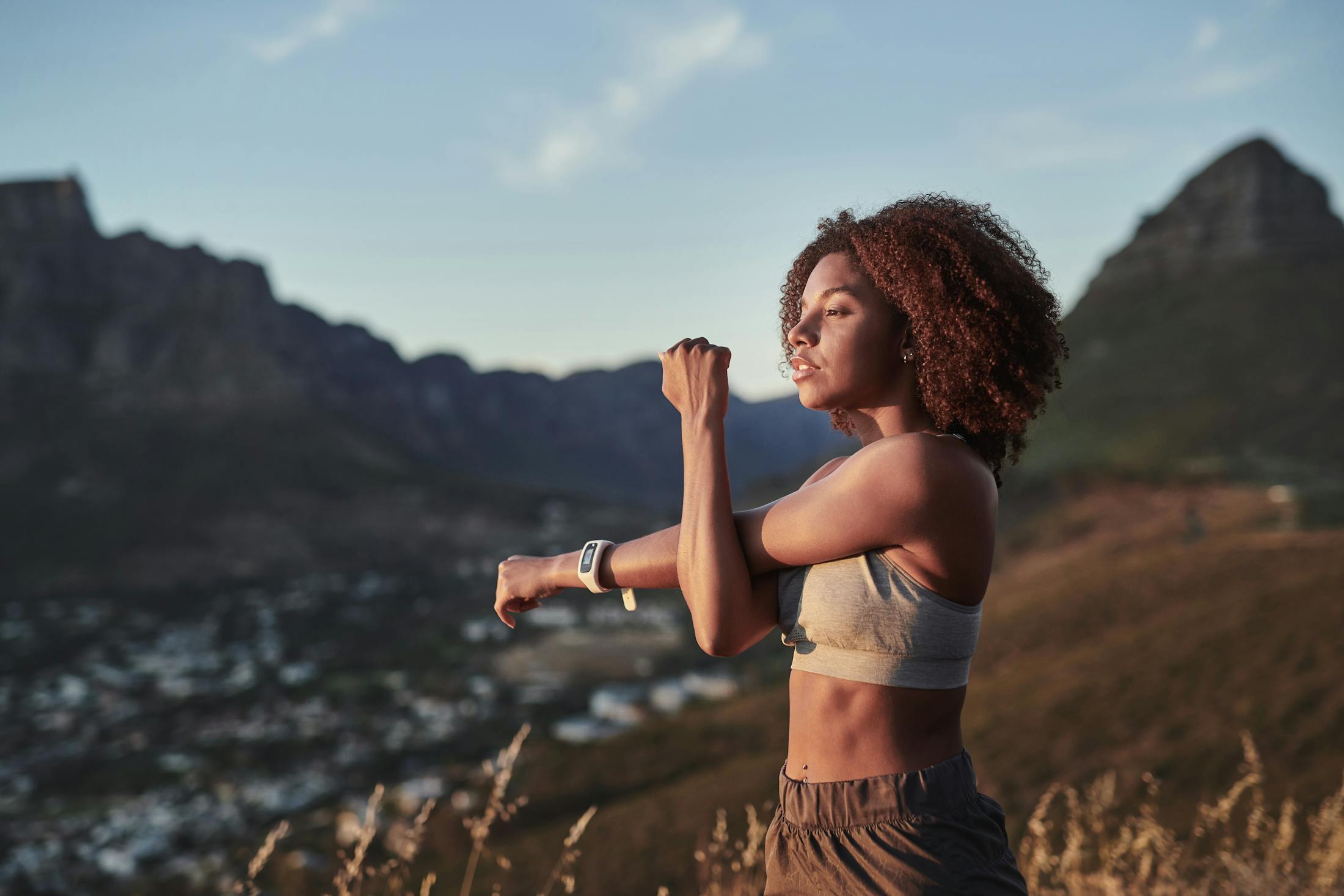 Woman on top of a hill, stretching her arms after a run while looking out at the view.