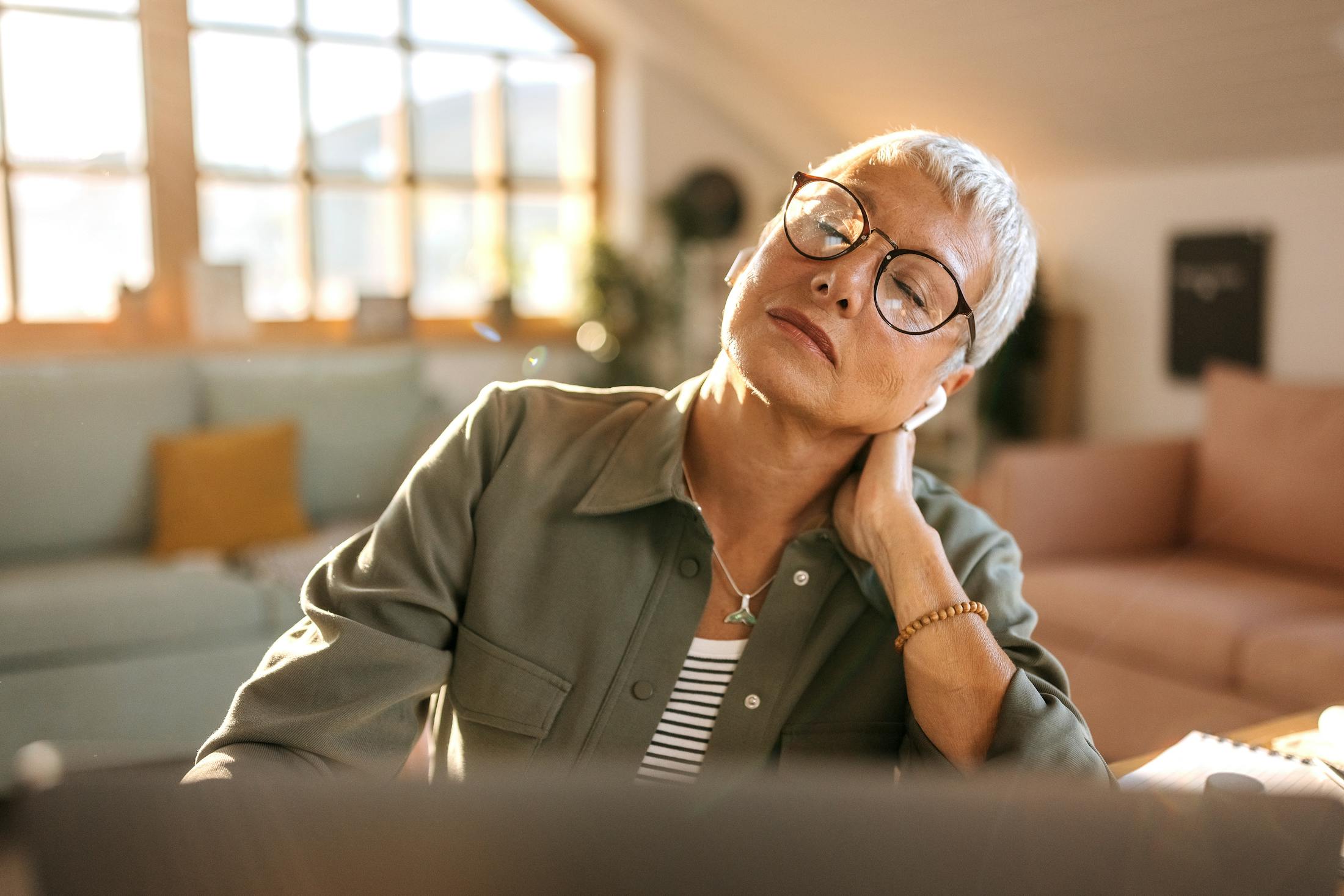 Older woman sitting by computer and rubbing her neck in pain.