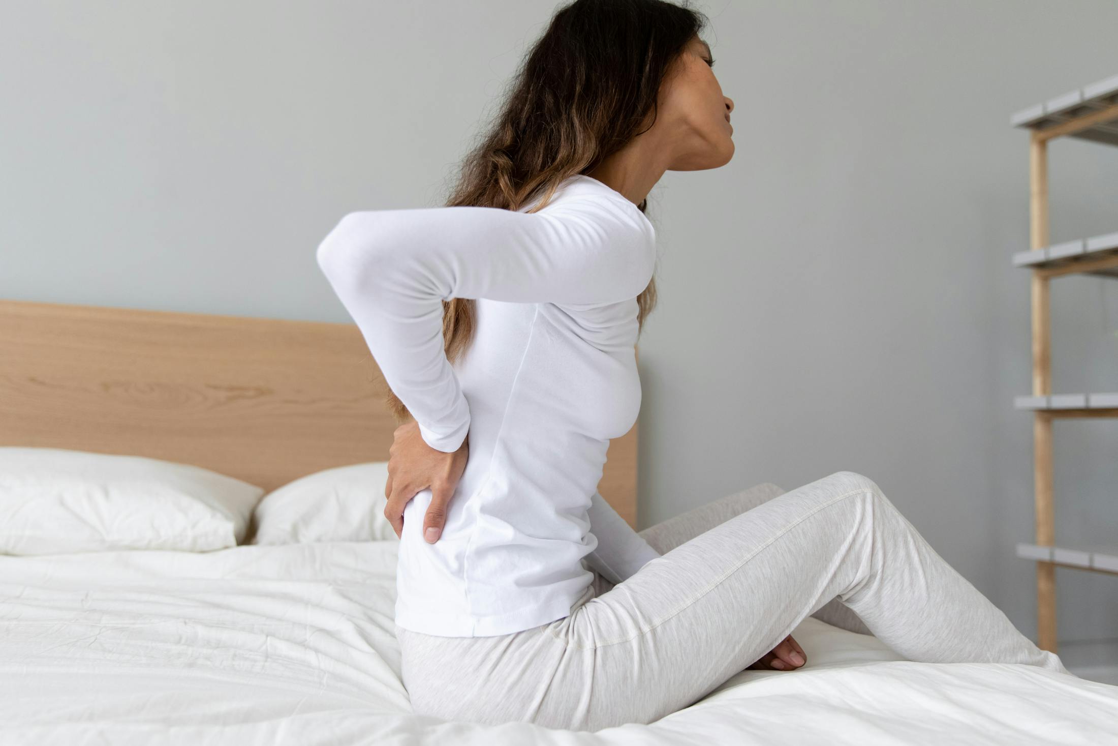 woman sitting on bed holding her back in pain from her Sciatica nerve