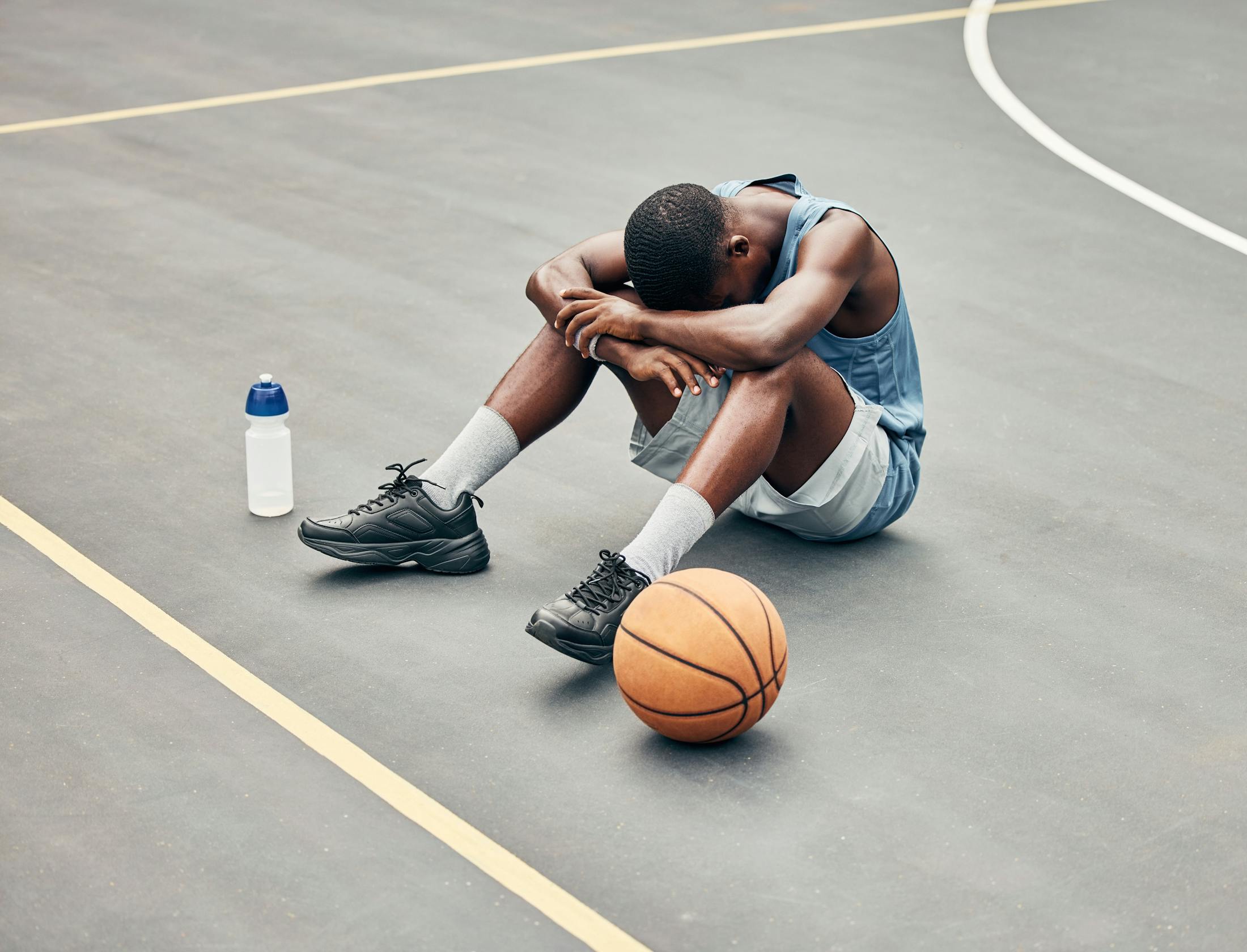 Man is on basketball court with head down on his arms due to an injury