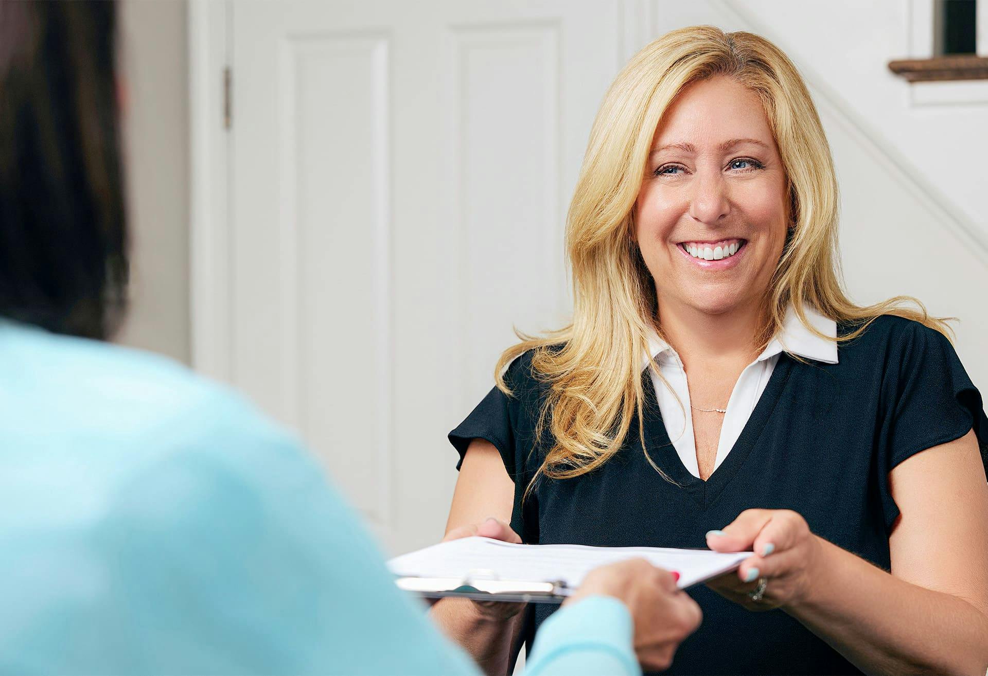 woman handing another woman a clipboard with paperwork to fill out