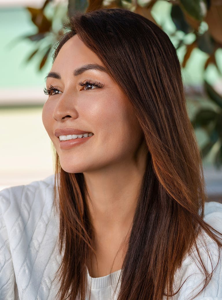 Woman with long hair and white sweater smiles looking to the side