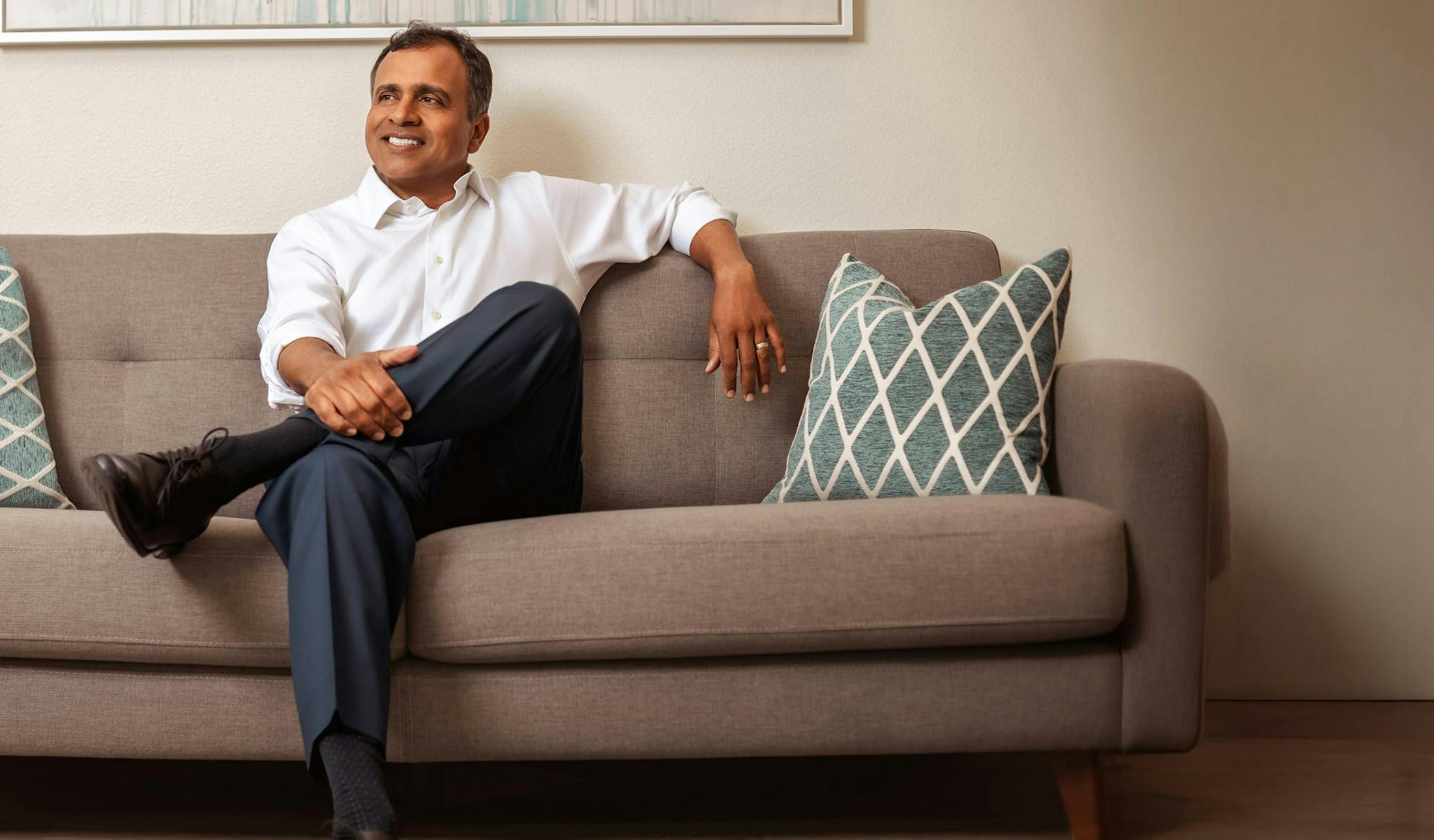 Dr. Gupta seated on a couch wearing white button down and navy pants