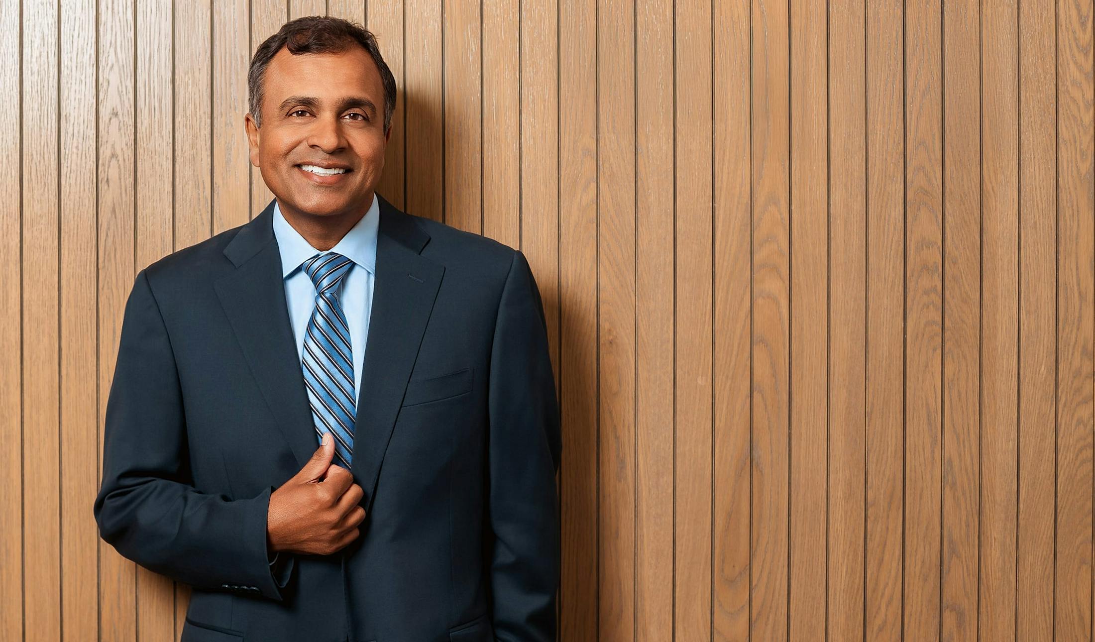 Dr. Gupta in a navy suit with blue striped tie