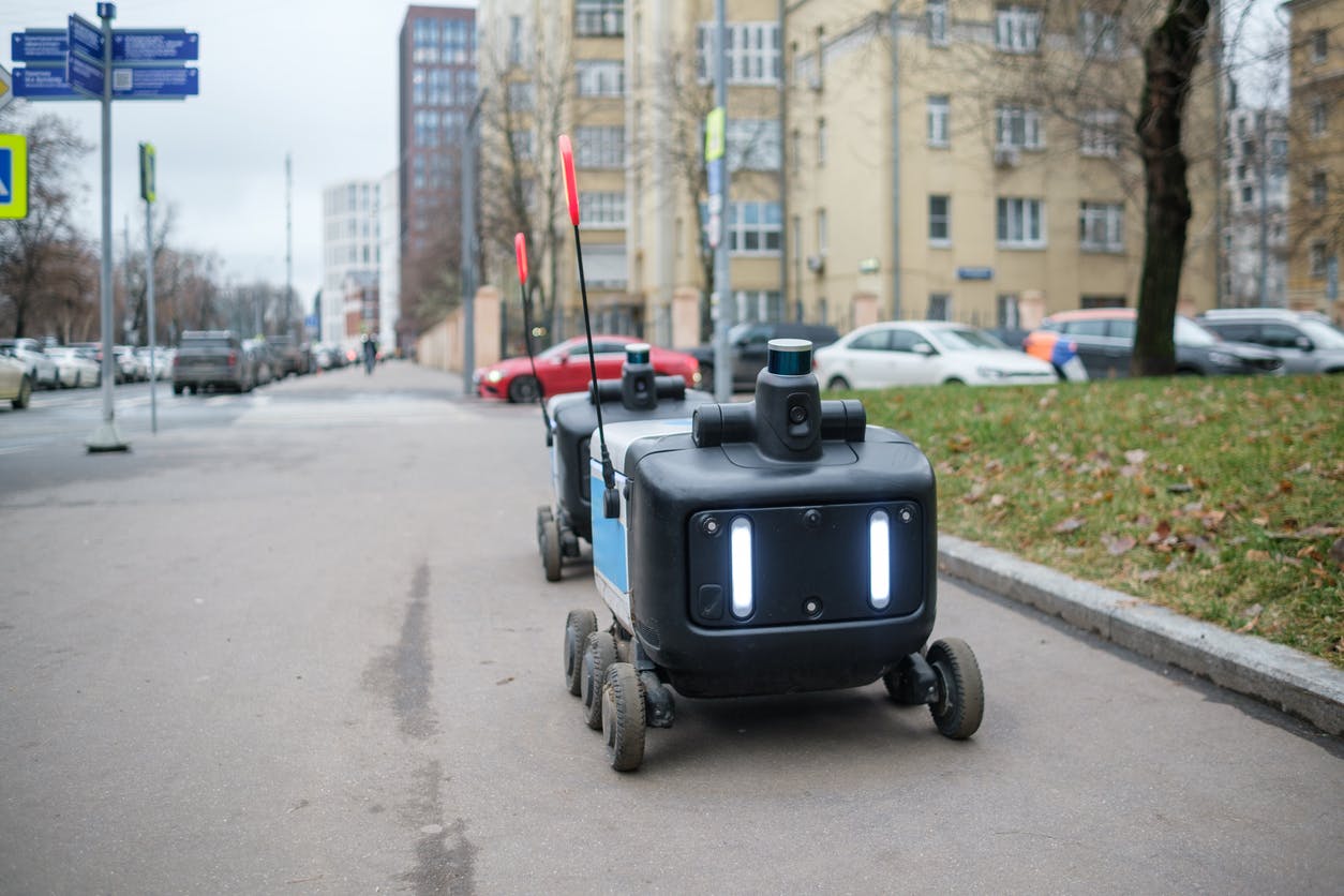 Two delivery robots navigate a city sidewalk