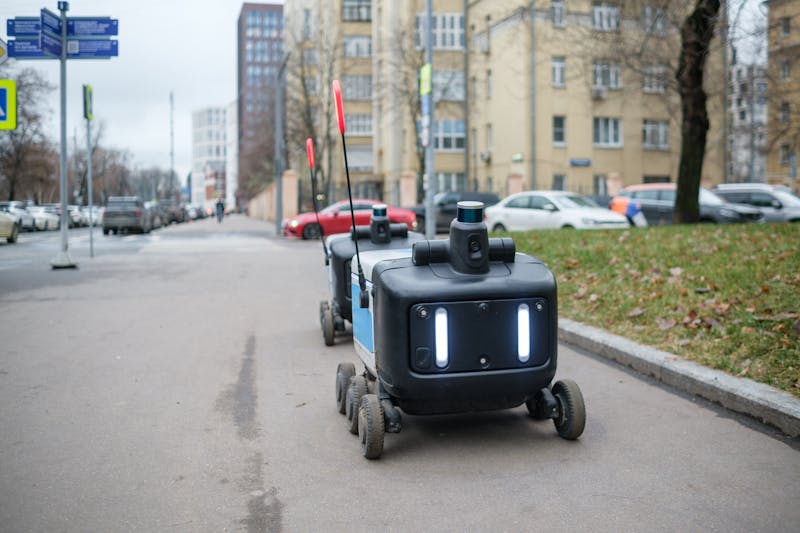 Two delivery robots navigate a city sidewalk