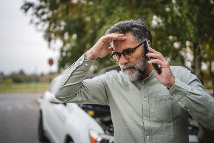 A stressed man on phone in front of his car