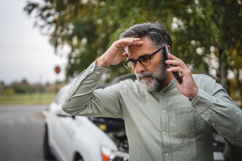 A stressed man on phone in front of his car