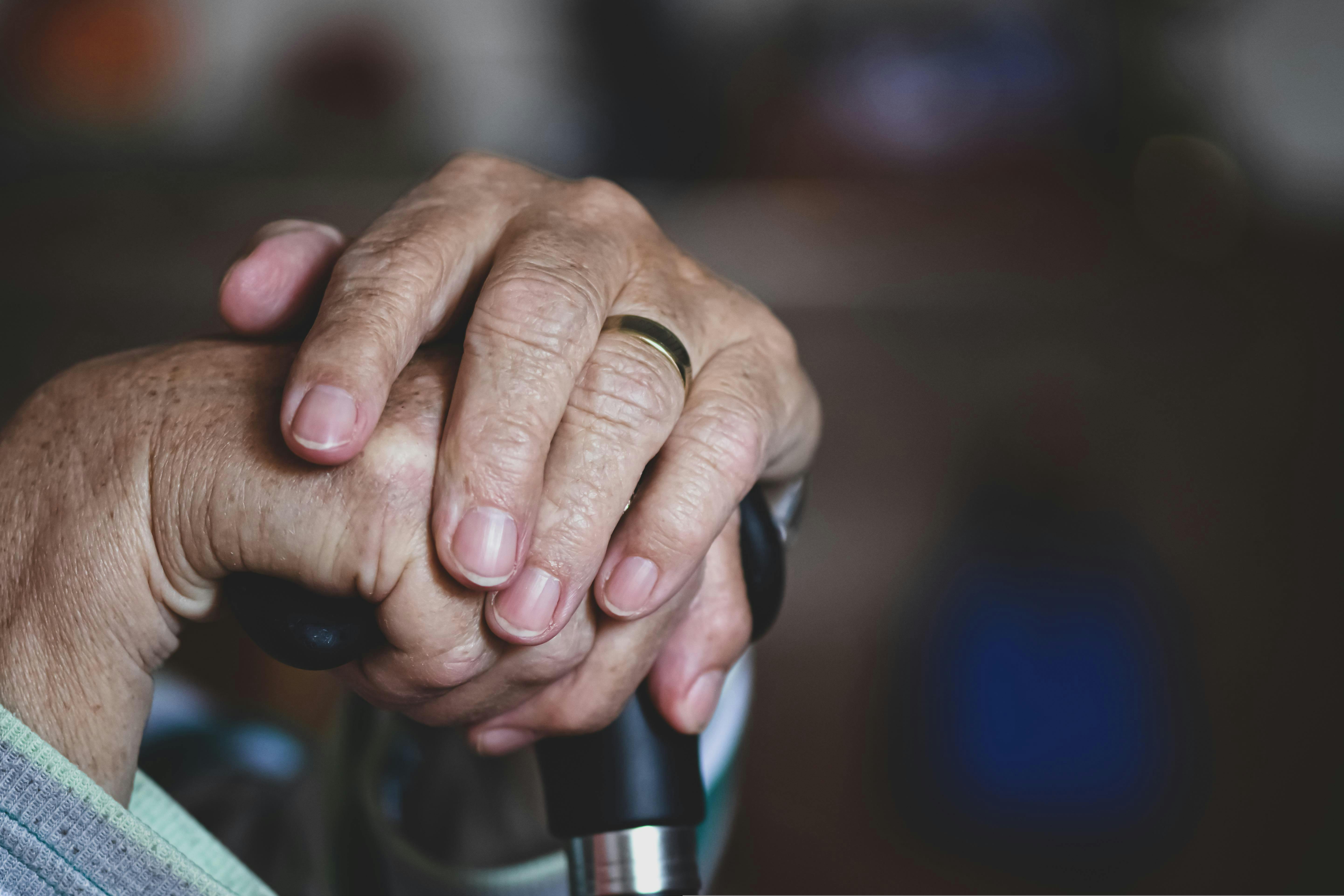 An old man's hands on top of a cane