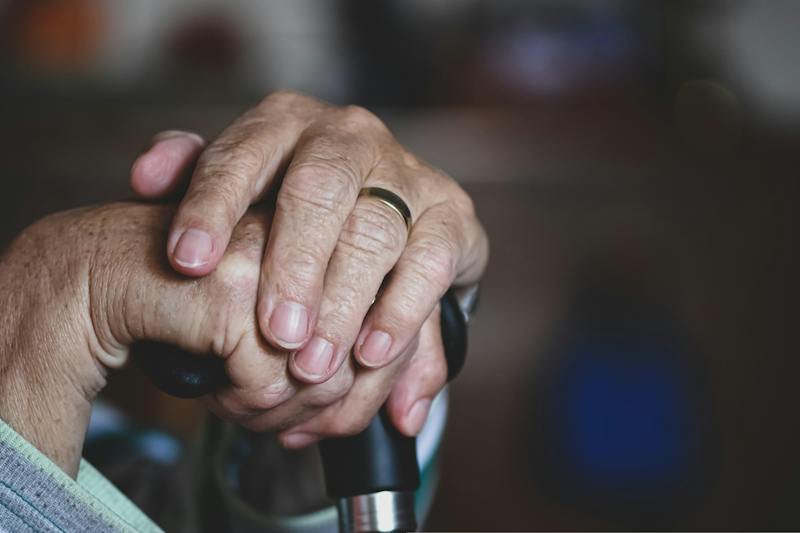 An old man's hands on top of a cane