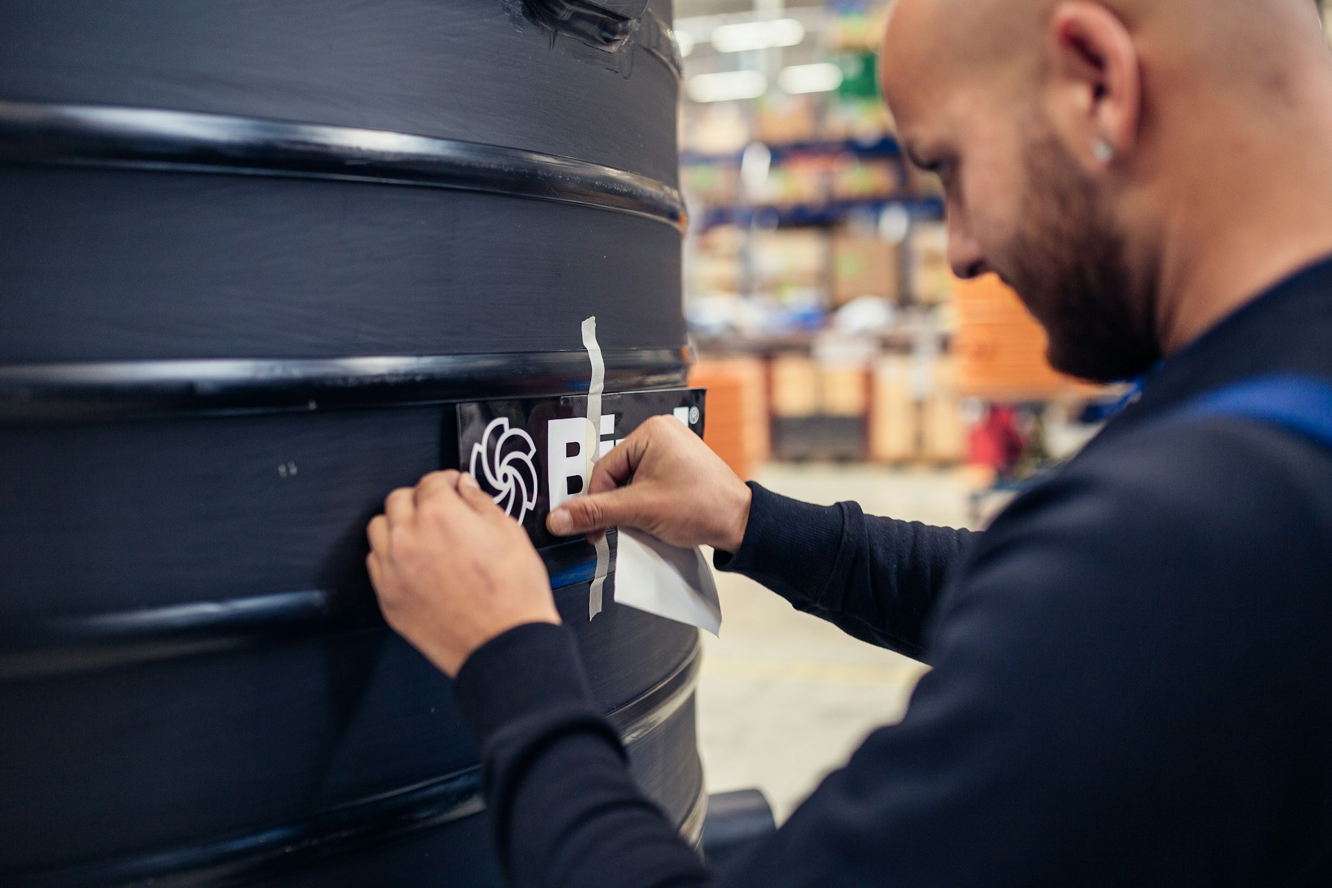 Mitarbeiter klebt Biral-Logo auf schwarzen Kunststoff-Pumpschacht im Produktionslager